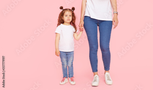 Family values. Mom and daughter in white t-shirts and jeans play and hug on a pink background. Caring for loved ones. Happy motherhood
