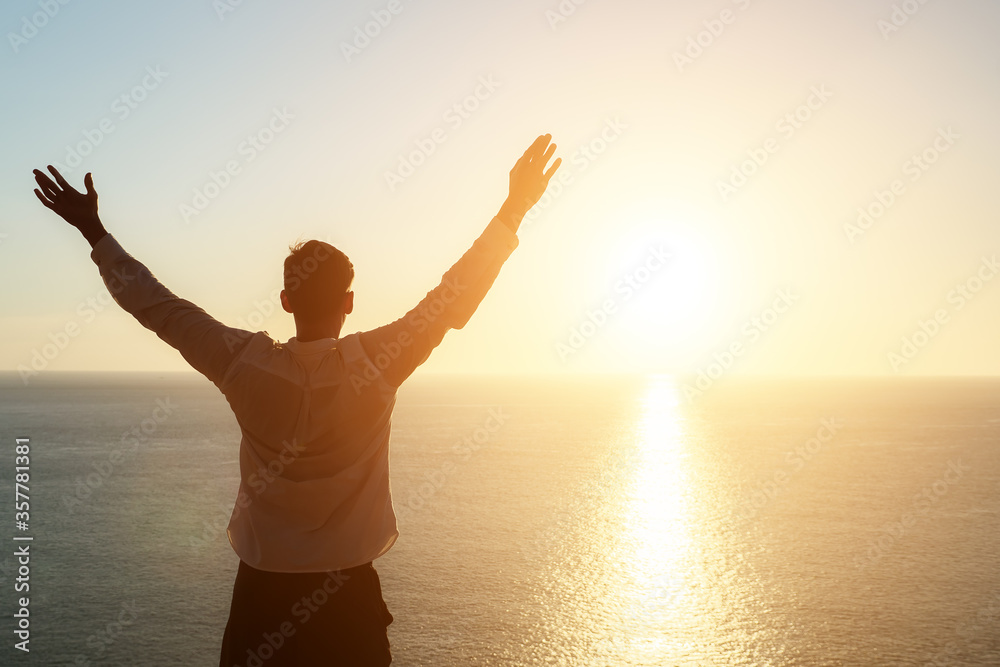 male silhouette raises hands and admires pictorial sunset standing on beach edge at sunset copyspace