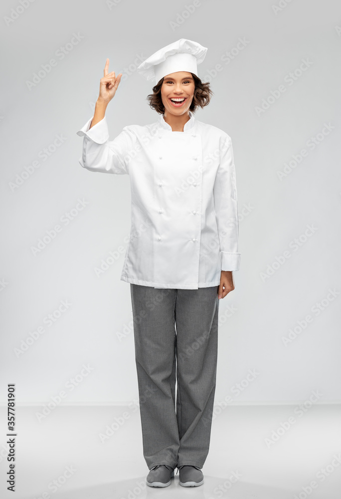 cooking, advertisement and food concept - happy smiling female chef in toque pointing finger up over grey background