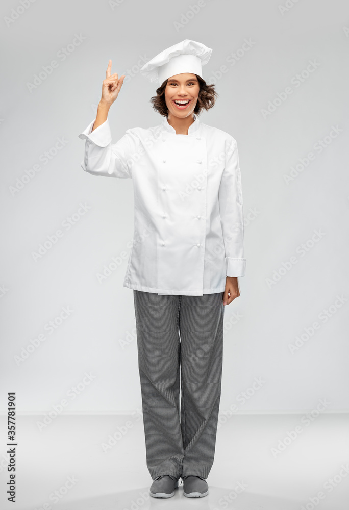 cooking, advertisement and food concept - happy smiling female chef in toque pointing finger up over grey background cooking, advertisement and food concept - happy smiling female chef in toque pointing finger up over grey background