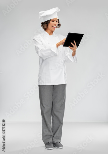 cooking, culinary and people concept - happy smiling female chef in toque with tablet pc computer over grey background