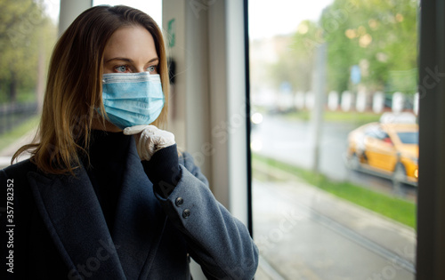 Pensive woman in medical mask standing at window in bus.