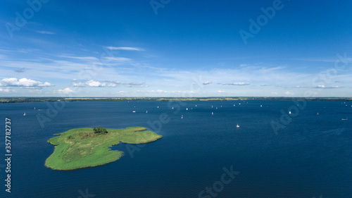 Aerial - multiple small sailboats on big lake Niegocin in Gizycko, Warmia-Masuria, Poland. Relaxation during sunny summer day. Green bird-island on lake. photo