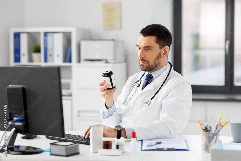 healthcare, medicine and people concept - male doctor with drug in jar and computer at hospital
