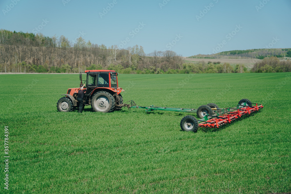 The tractor is working on a green spring field. Agriculture with cereal crops The tractor is working on a green spring field. Agriculture with cereal crops