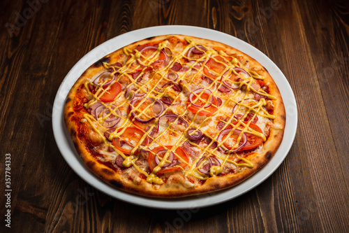 Bacon, sausage, onion, tomato nourishing pizza with cheese sauce, wooden background, low key