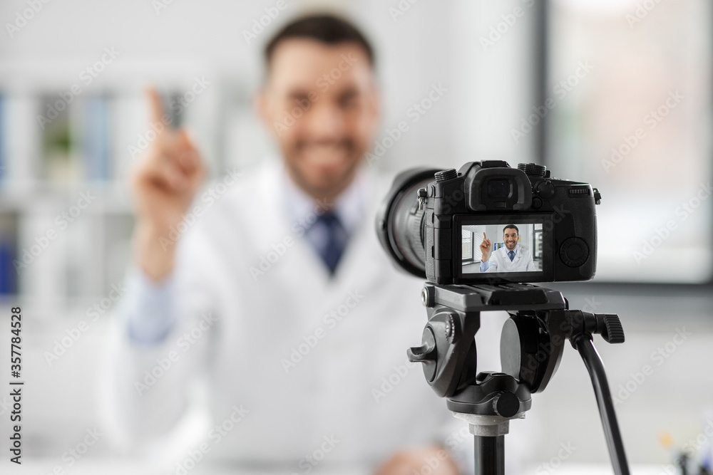 healthcare, medicine and blogging concept - happy smiling male doctor with camera recording video blog at hospital