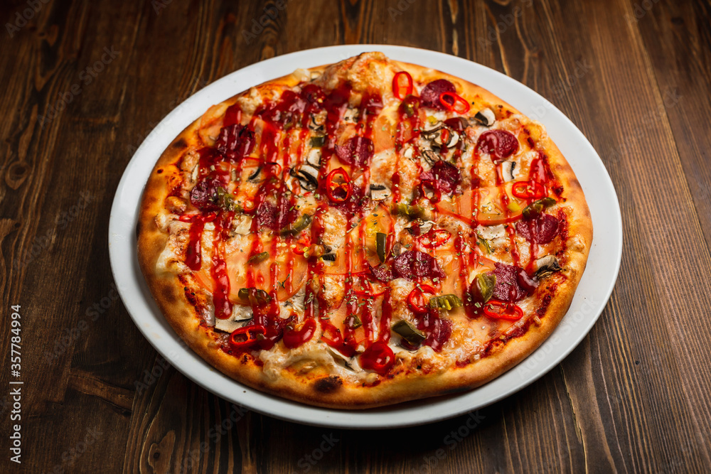 Pepperoni, mushroom, tomato, jalapeno and chili pepper and cheese spicy pizza with barbeque sauce, wooden background, low key