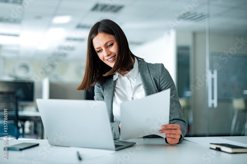 Portrait of a cheerful entrepreneur working with laptop and documents.