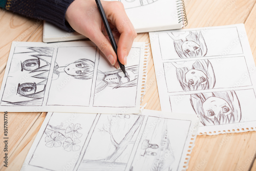Artist drawing an anime comic book in a studio. Wooden desk, natural light. Creativity and inspiration concept. Artist drawing an anime comic book in a studio. Wooden desk, natural light. Creativity and inspiration concept.