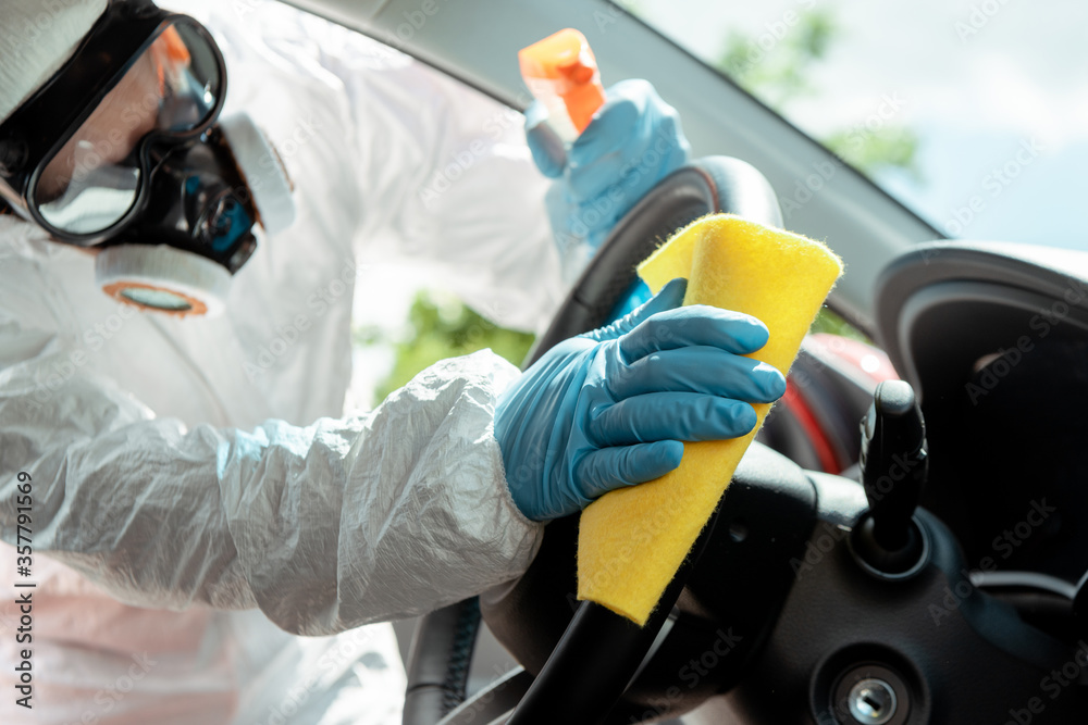 Fototapeta premium specialist in hazmat suit and respirator cleaning car interior with antiseptic spray and rag during covid-19 pandemic