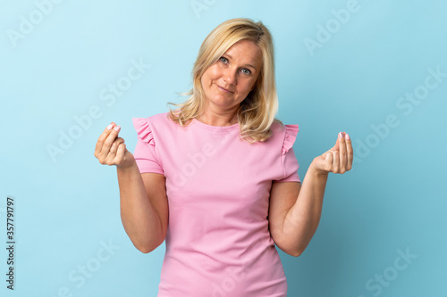 Middle age woman isolated on blue background making money gesture © luismolinero