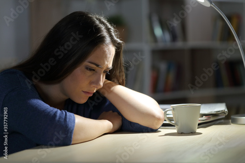 Sad woman complains sitting on a desk at night at home