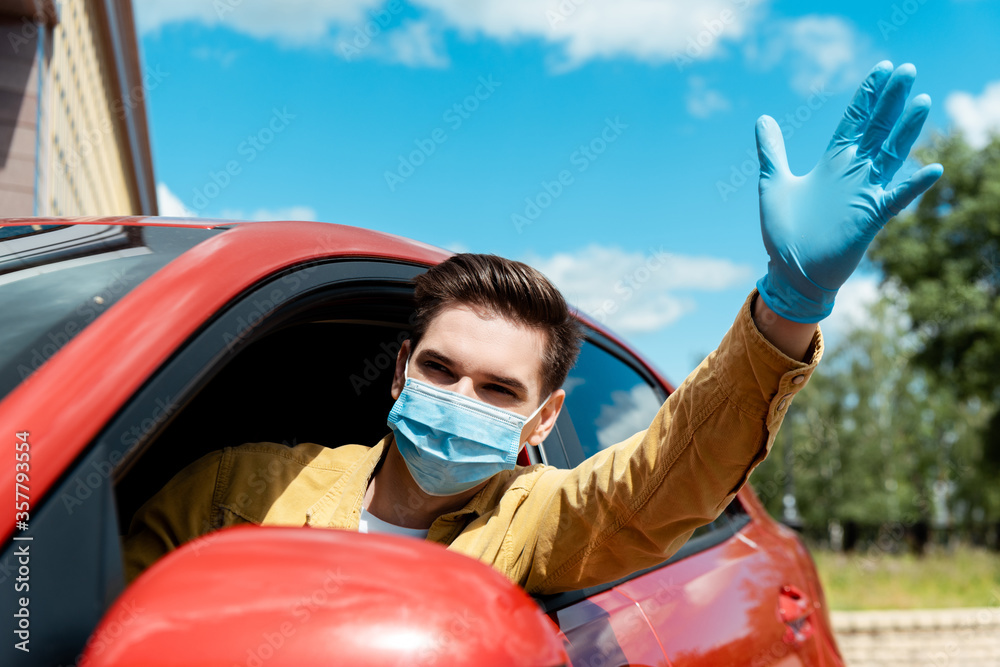 Naklejka premium man in medical mask and protective gloves waving and driving taxi during covid-19 pandemic