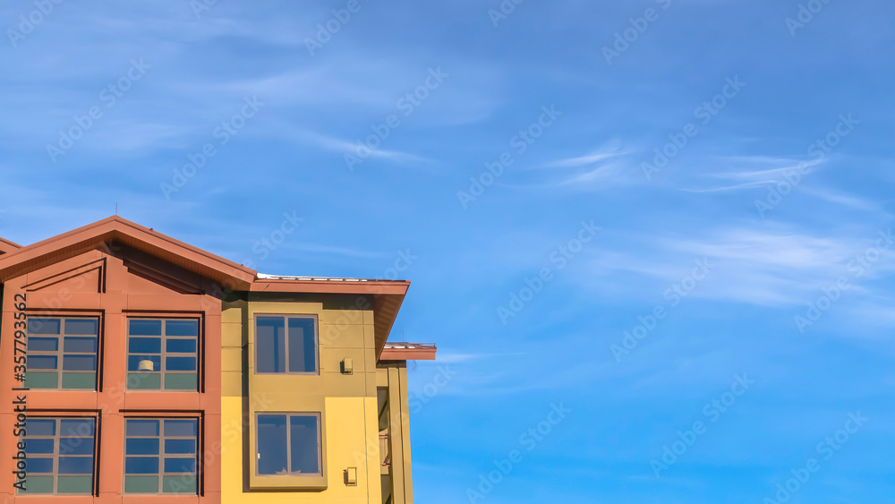 Panorama crop Home exterior with balconies and multi color walls against blue sky and clouds Panorama crop Home exterior with balconies and multi color walls against blue sky and clouds