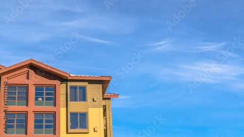 Panorama crop Home exterior with balconies and multi color walls against blue sky and clouds
