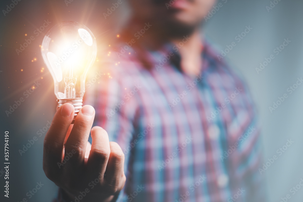 Idea innovation and inspiration concept.Hand of man holding illuminated light bulb, concept creativity with bulbs that shine glitter.Inspiration of ideas for sustainable business development. - obrazy, fototapety, plakaty 