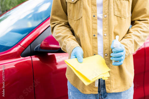 cropped view of young man in latex gloves using antiseptic and rag for cleaning car during coronavirus pandemic