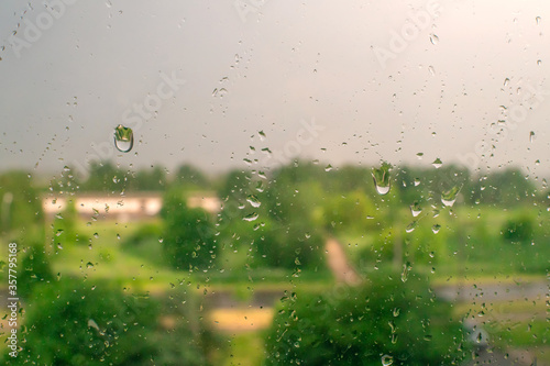 Raindrops on a window with green trees and a cloudy sky in the background on a summer day
