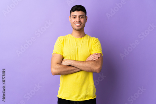 Young Colombian man isolated on purple background keeping the arms crossed in frontal position