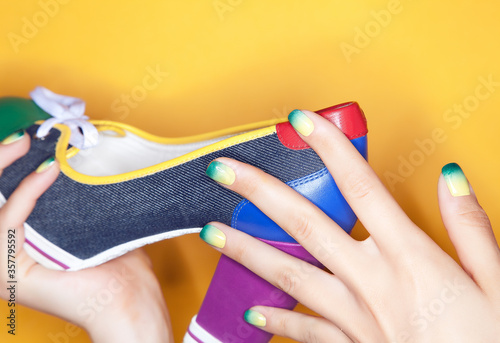 Close-up shot of a beautiful female hands with a luxurious green ombre manicure holding a multicolored shoe on a yellow background