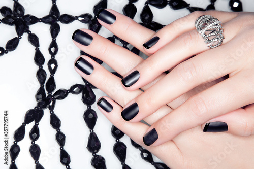 Close-up shot of beautiful female hands with black manicure on white background with black crystal beads