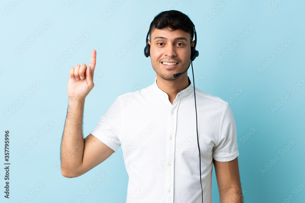 Telemarketer Colombian man working with a headset over isolated background pointing up a great idea