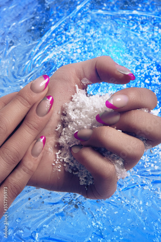 Close-up shot of beautiful female hands with colored manicure on blue icy background