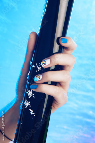 Close-up shot of a beautiful female hand with colored manicure holding a black tube on a blue ice background
