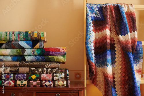 Stack of quilts and quilt made in the bargello style on yellow wall background photo