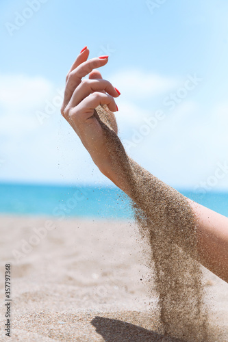 Female hand with manicure on nails on the beach with beautiful sand