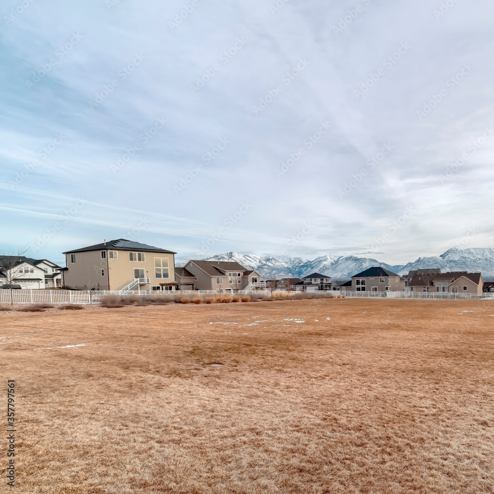 Square crop Grassy field with melting snow against homes and snowy mountain background