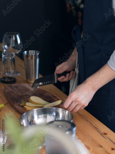 A man cook cooks in the kitchen in a blue apron, cuts a knife on the board with fruit