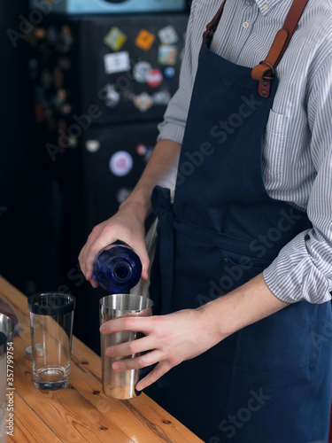 A man cook in a blue apron is cooking in the kitchen, the process of preparing a cocktail
