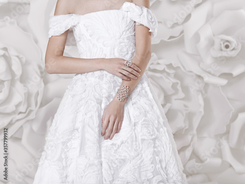 Beautiful luxurious girl in a white lace wedding dress with flowers and beautiful jewelry, on the background with large white flowers