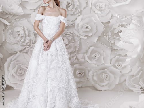 Beautiful luxurious girl in a white lace wedding dress with flowers and beautiful jewelry, on the background with large white flowers