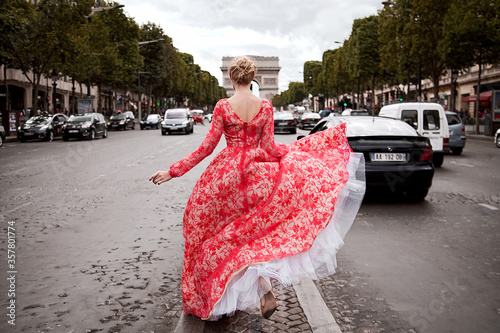 A beautiful young woman runs in a luxurious peach long dress on the middle of the road in Paris, looks at the Arc de Triomphe