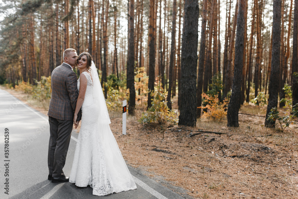 Groom kissing smiling bride while standing in the pines forest. Bride and groom portrait