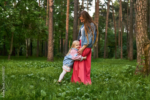 happy child girl hugs her mom standing on the grass in the park