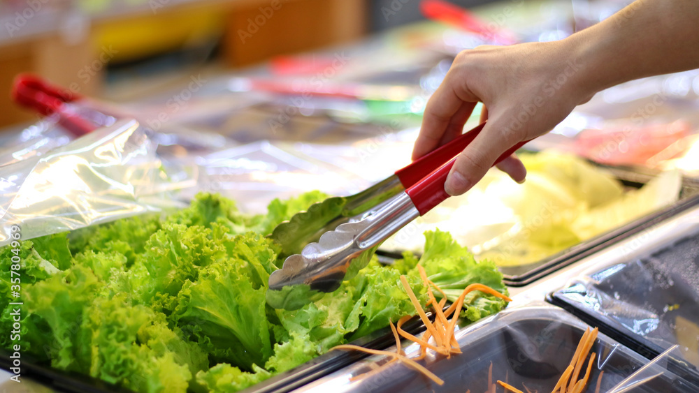 Obraz premium Someone's hand picking or choosing vegetable (Lettuce) by using tongs on salad bar at supermarket