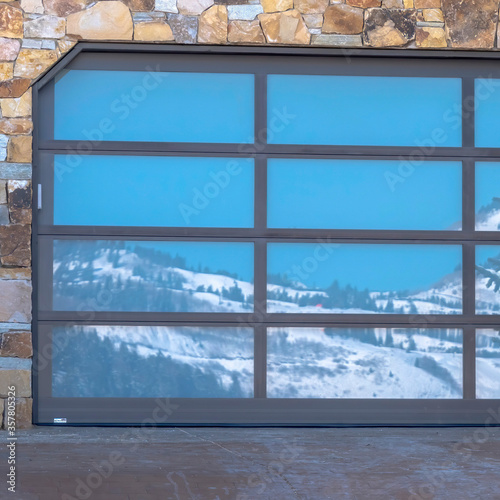 Square frame Garage door with glass panes reflecting a snowy hill landscape under blue sky