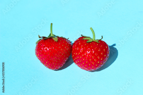 Two red srawberries on blue background. Abstract food backdrop. Food, dessert, color concept. Red berries, blue backdrop.   photo