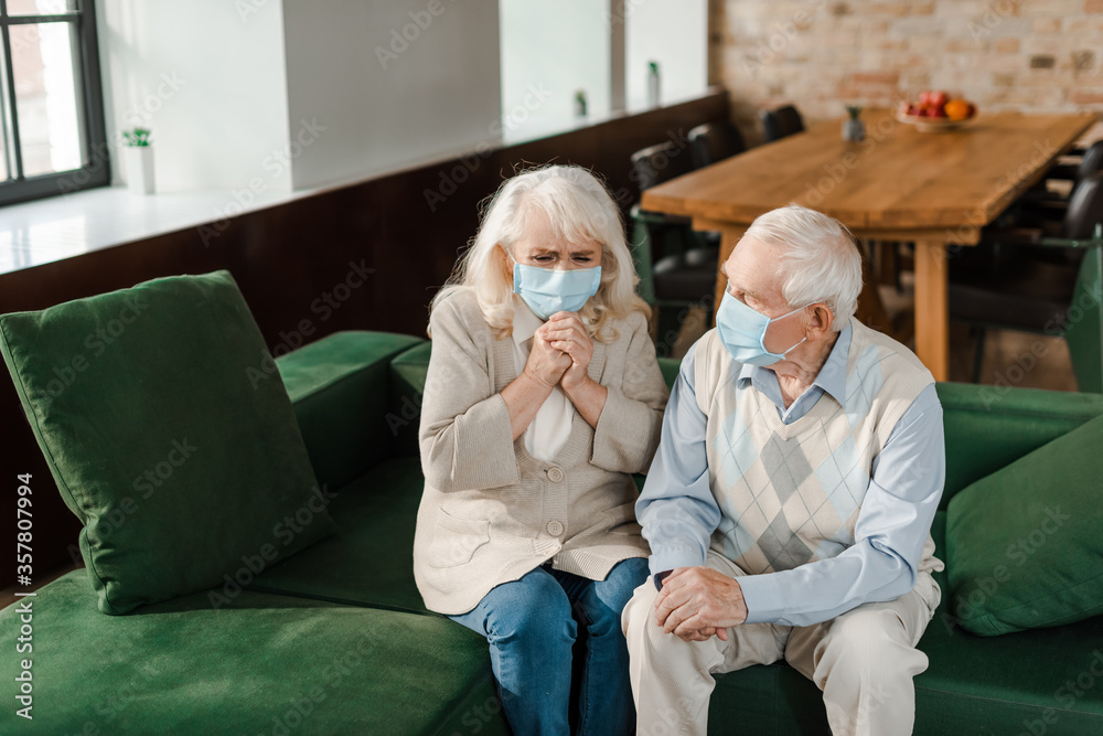 ill elderly wife and husband in medical masks sitting on sofa during coronavirus epidemic ill elderly wife and husband in medical masks sitting on sofa during coronavirus epidemic
