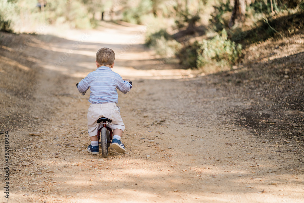 Back of cute toddler riding bicycle on dirt road Back of cute toddler riding bicycle on dirt road