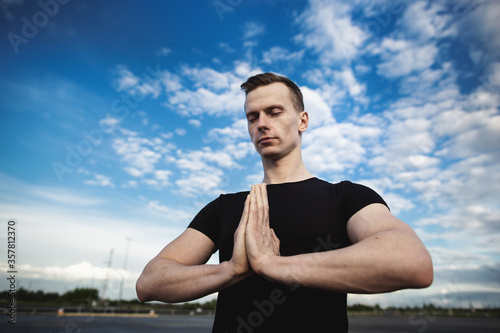 Close-up portrait of a young man practicing yoga on a background of blue sky with clouds.