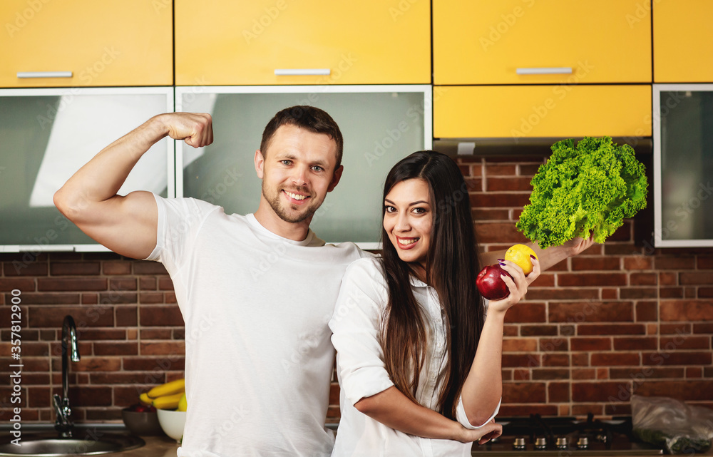 Obraz premium Happy friends preparing food for dinner, posing in the kitchen holding vegetables and fruits. Promoting healthy eating
