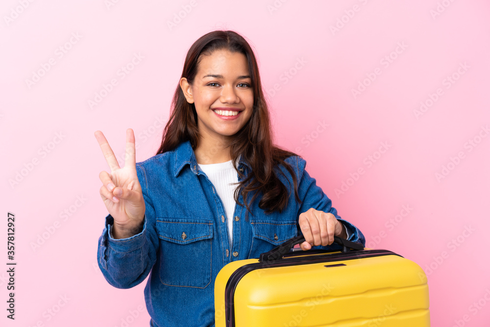 Traveler Colombian woman holding a suitcase over isolated pink background smiling and showing victory sign Traveler Colombian woman holding a suitcase over isolated pink background smiling and showing victory sign