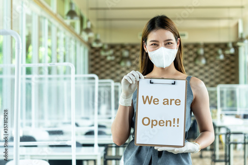 Wman restaurant owner wear mask and glove holding sign reopen the restaurant after closed from city lock down decorated with screen for customer seperation for covid protection policy