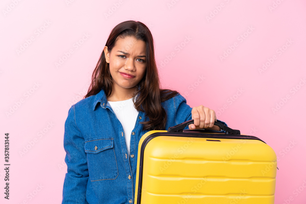 Traveler Colombian woman holding a suitcase over isolated pink background with sad expression Traveler Colombian woman holding a suitcase over isolated pink background with sad expression