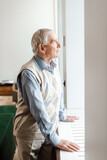 upset elderly man standing and looking through window during quarantine